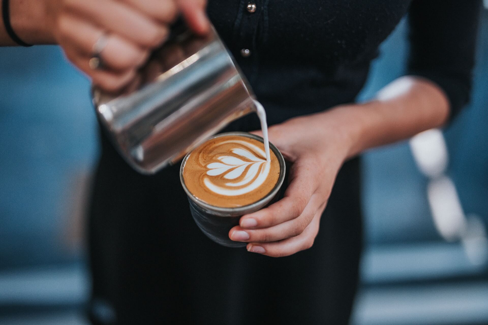 Barista pouring milk into coffee cup making pattern on top